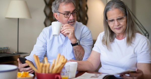 Older married couple sitting together at breakfast table, each absorbed in their own phone, not connecting