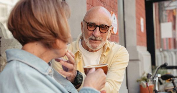 Older couple leaning in toward each other over coffee in conversation outside a cafe
