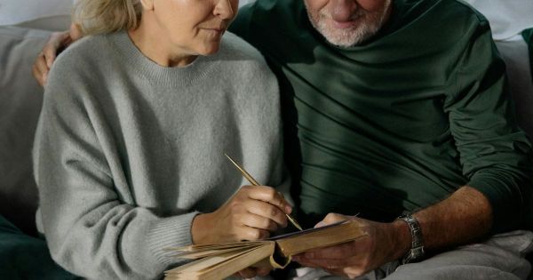 Older couple sitting close together on couch as woman writes in notebook suggesting intentional planning and partnership
