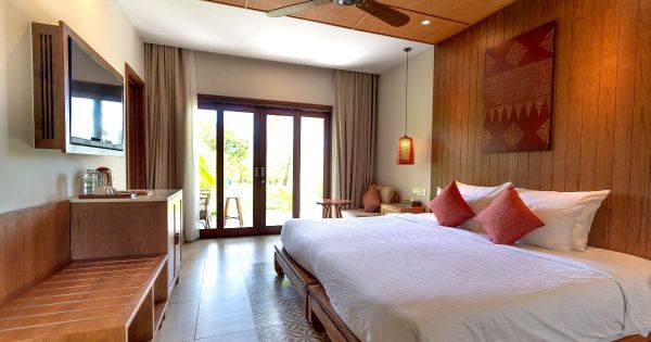 Warm wood hotel room with king bed, rose pillows and tropical garden view
