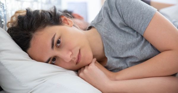 Woman lying awake in bed, distant from her partner, holding herself