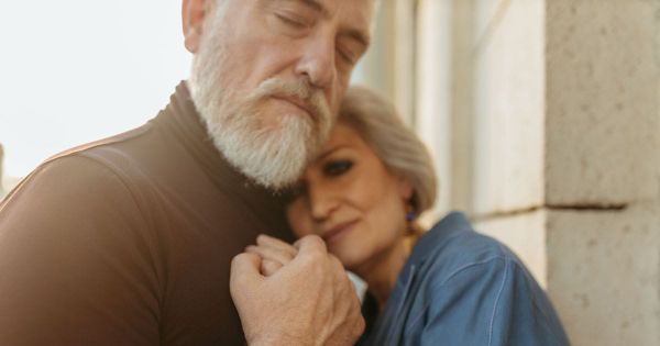 Older couple holding each other close in warm light, a quiet moment of tenderness and connection