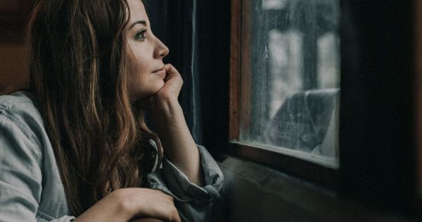 Woman resting her chin on her hand gazing out a rain-streaked window, lost in thought