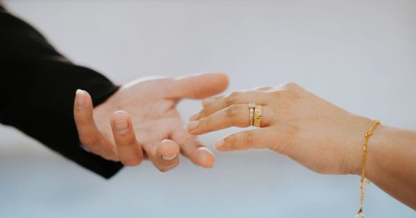 Two hands reaching toward each other, wedding rings visible.