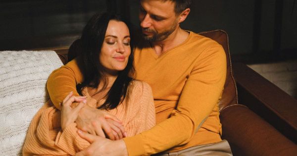 Couple resting together on a couch, her eyes closed, hands clasped.