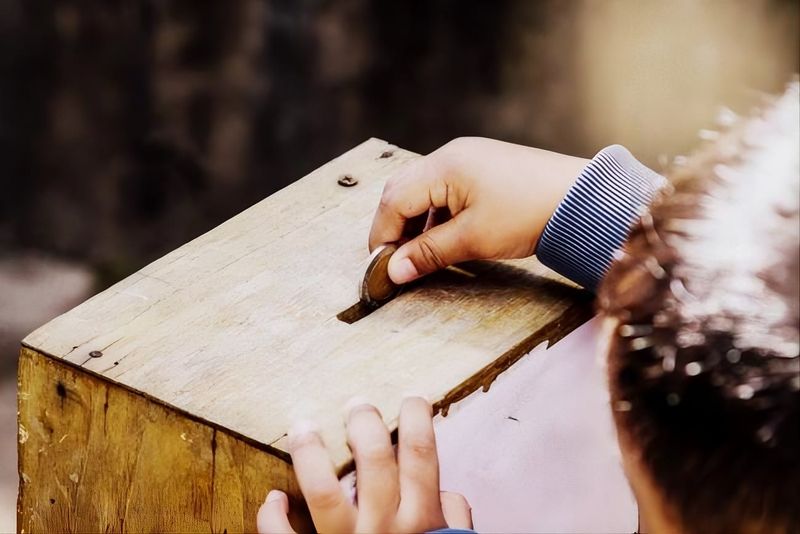 Pessoa colocando moeda em caixa de oferta de madeira durante contribuição na igreja