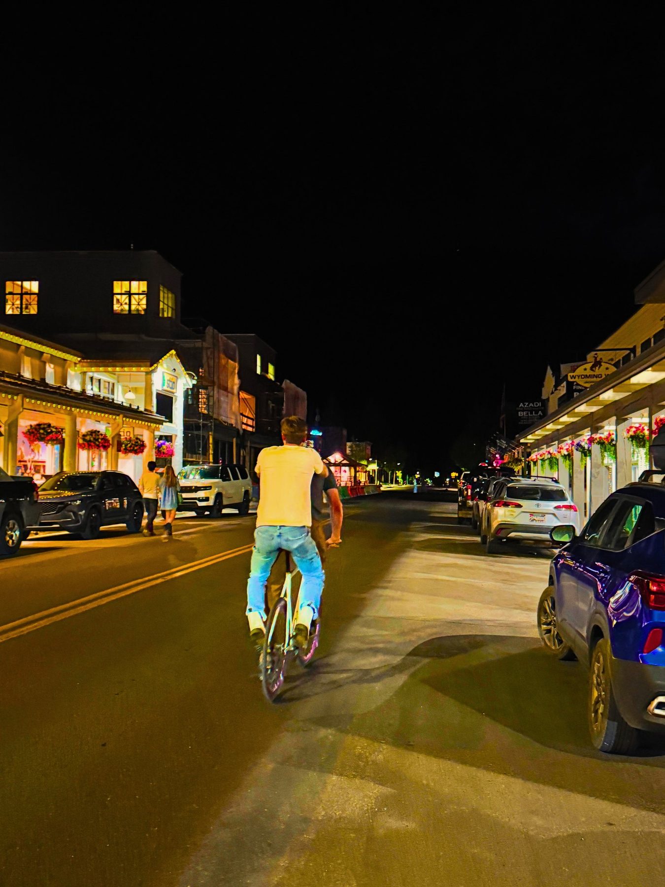From Kara Hobby’s Wilson Mom summer: cyclist riding down a lit main street at night