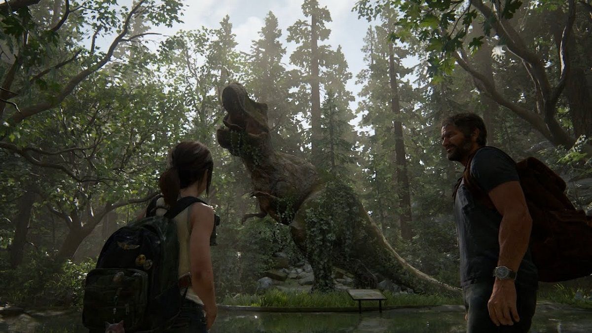 Ellie and Joel stand in front of a statue of a tyrannosaurus rex in an overgrown wooded area. Ellie has her back to the camera. Her brown hair is in a ponytail, and she's wearing a light tank top and a backpack. Joel is standing in profile looking at her. He is a white man with short brown hair and a beard. He's wearing a blue t-shirt a watch, jeans, and a backpack.