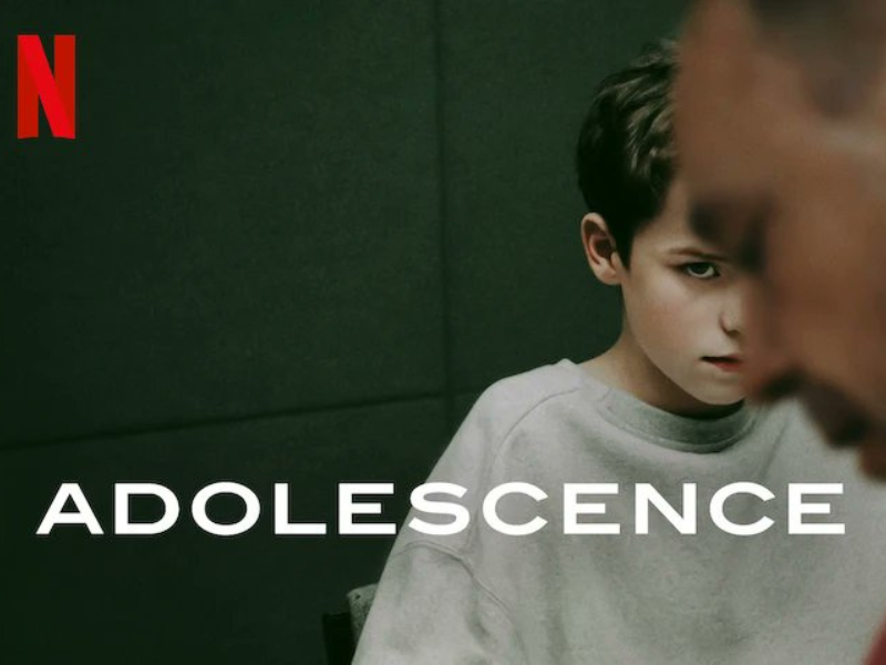 promotional image for the Netflix show 'Adolescence,' featuring a 13-year-old-boy in a grey sweatshirt looking up at his father, who's out of focus