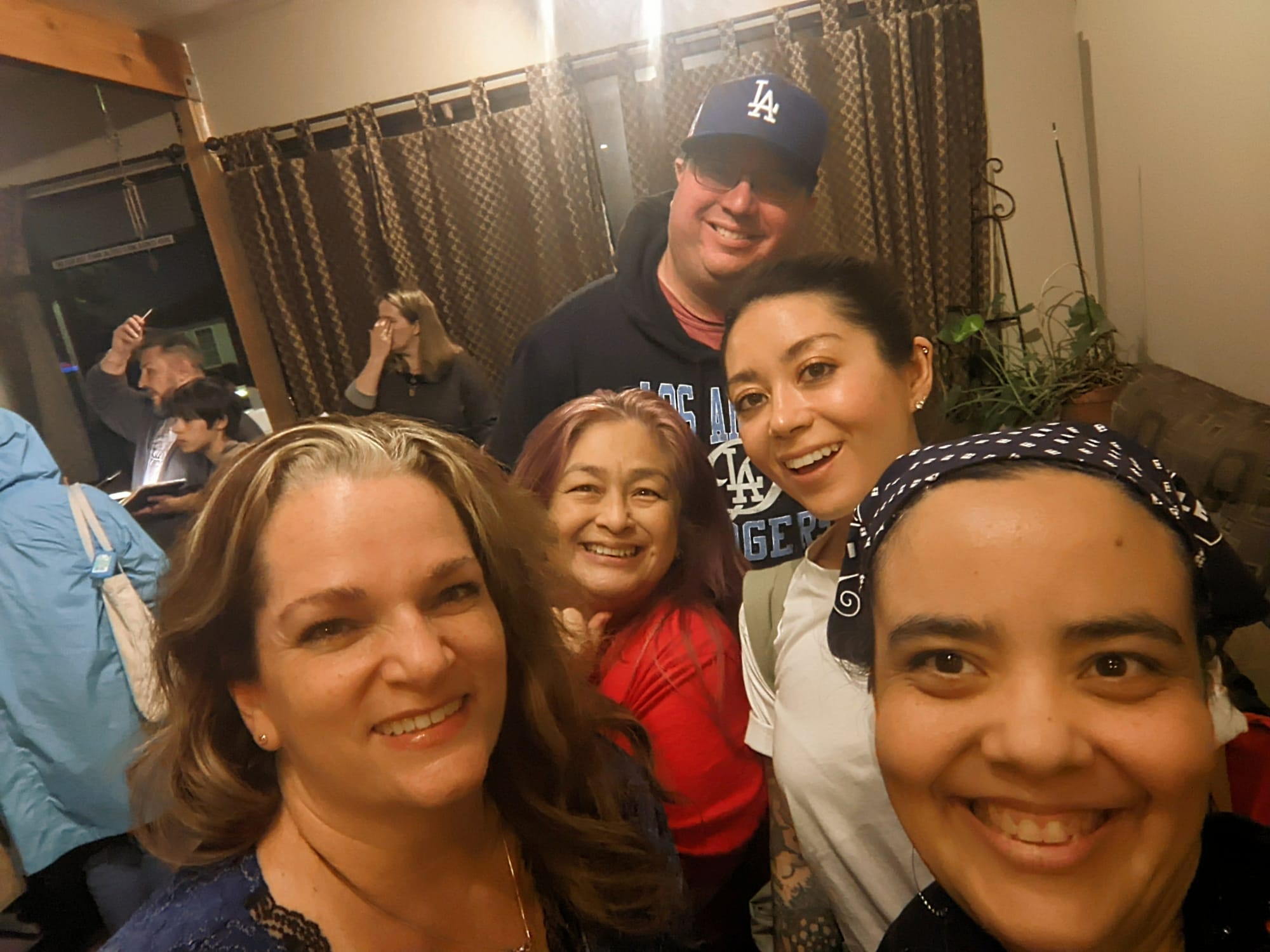 Image of five people (four women and one man) posed in a huddle for a selfie in a crowded room.