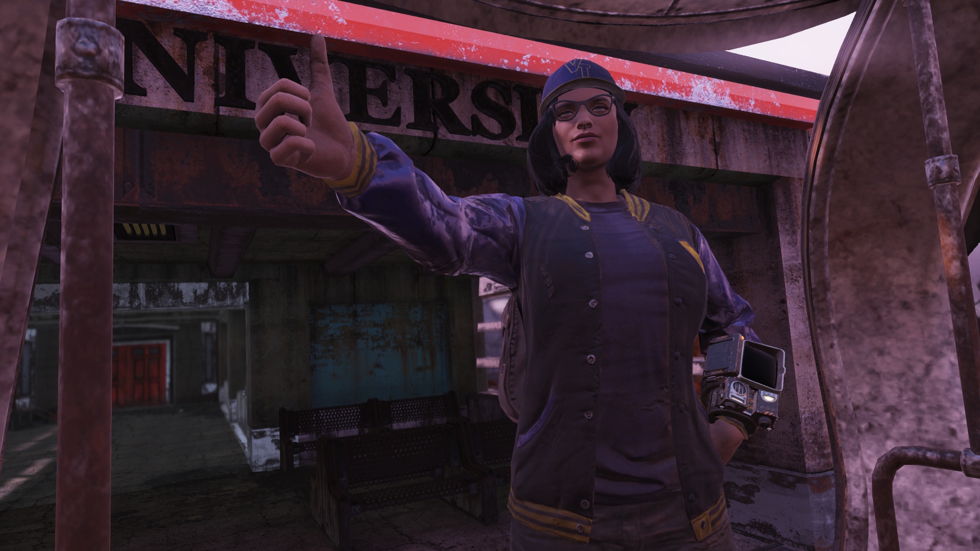 A female, brunette player character in 'Fallout 76' wearing a Vault-Tec University baseball cap, glasses, a varsity jacket, a Pip-Boy on her wrist, and jeans as she gives a thumbs-up in front of Vault-Tec University.
