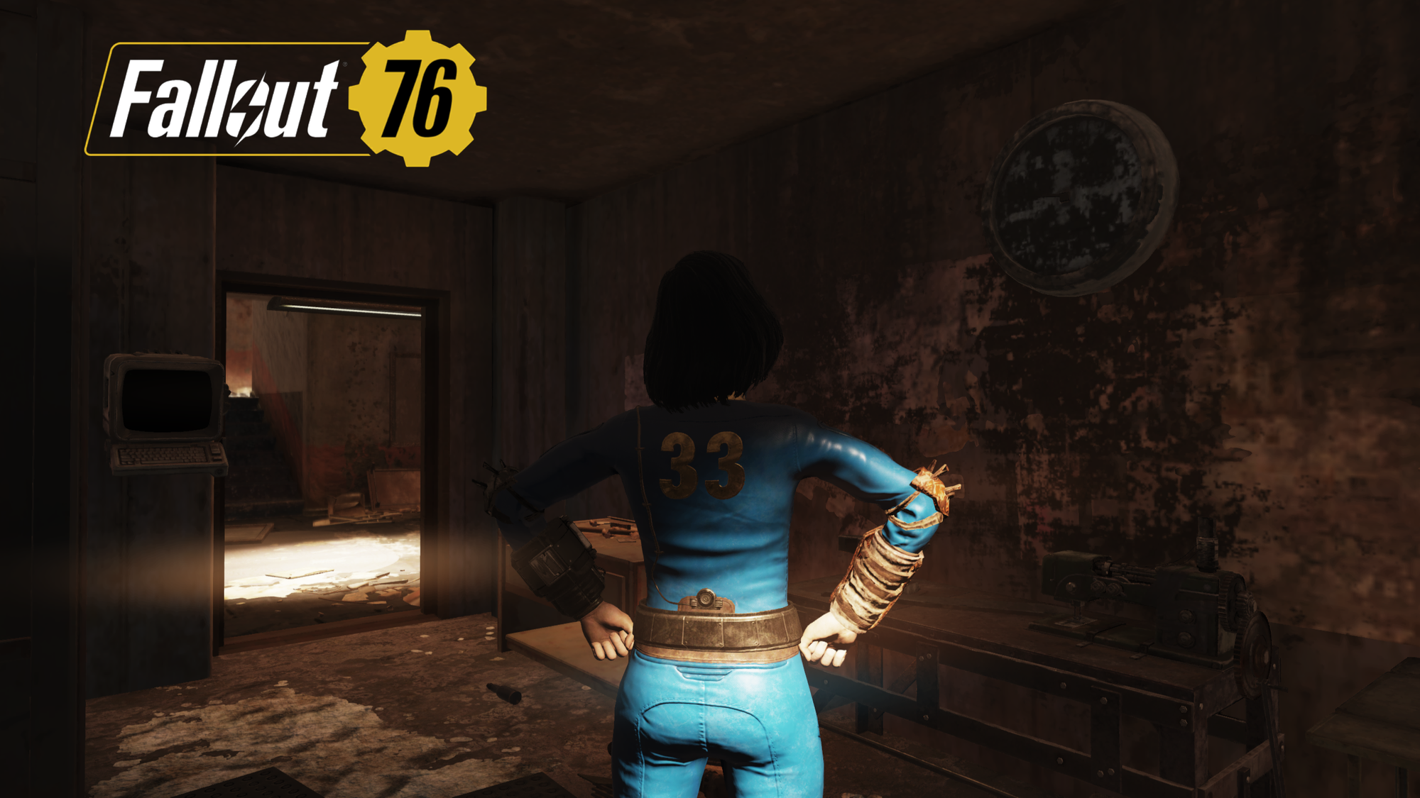 Image of a female, brunette player character with her back to the camera in 'Fallout 76' wearing a Vault 33 jumpsuit with her hands on her hips. The 'Fallout 76' logo is in the upper left-hand corner.