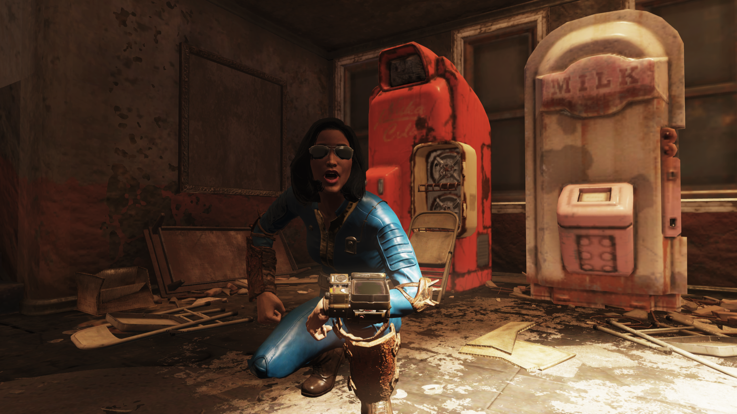 Female, brunette player character in 'Fallout 76' wearing sunglasses, a blue jumpsuit, and a Pip-Boy on her wrist crouching with a shocked look on her face in front of a Nuka-Cola machine and a Milk dispensing machine. 