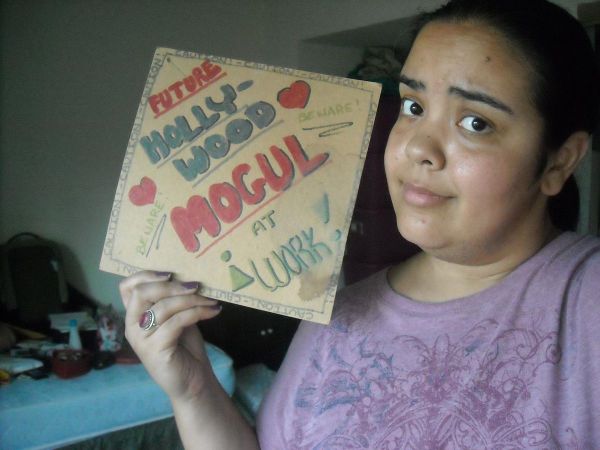 Image of me holding up a sign I made when I was 10 that reads "Future Hollywood Mogul at Work!"