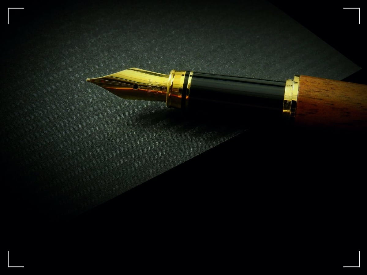 Detailed close-up of a classic fountain pen nib on textured black paper, showcasing elegance.