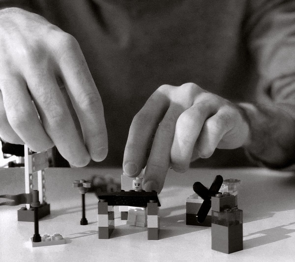 A man's hand playing with lego. This iluustrates that bulding upon others is why we need to share.