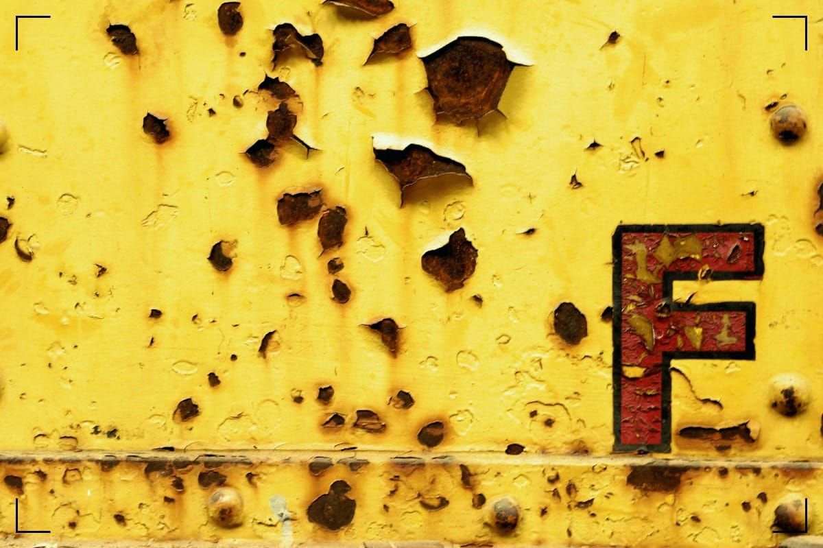 The letter "F" on a yellow background that looks like the side of a truck. The paint isfalling off and rust is visible.