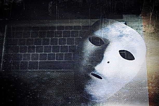A white theatrical mask resting face-up on a laptop keyboard, spectral and unnerving. 