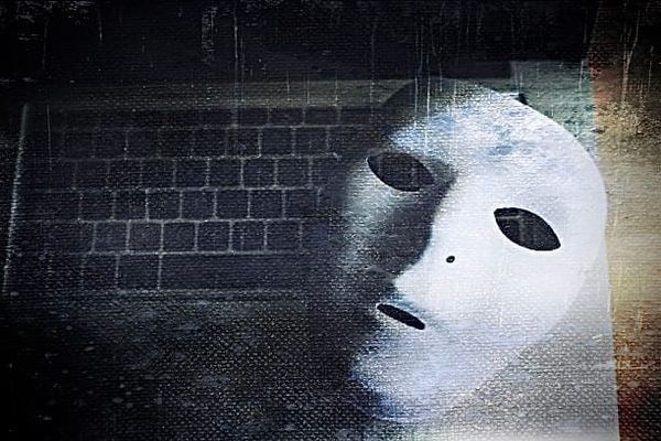 A white theatrical mask resting face-up on a laptop keyboard, spectral and unnerving. 