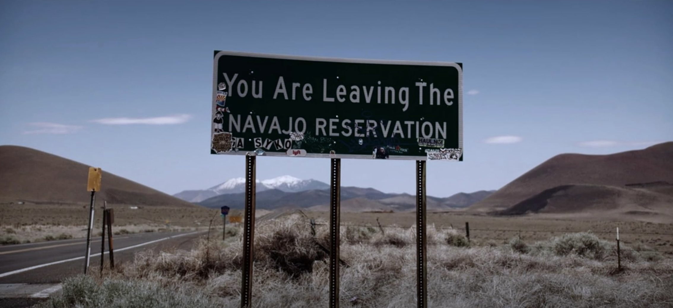 a street sign along a desert road reads, You Are Leaving The Navajo Reservation"