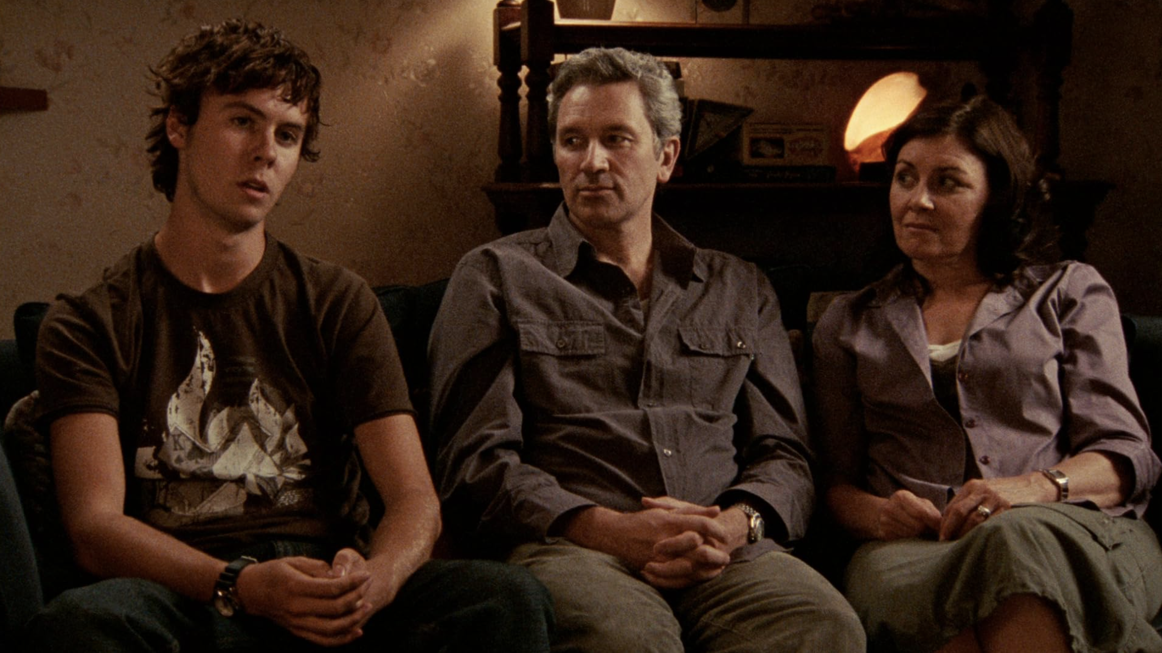 A family sits on chairs during a documentary interview. The mother and father look at their teenage son as he speaks.