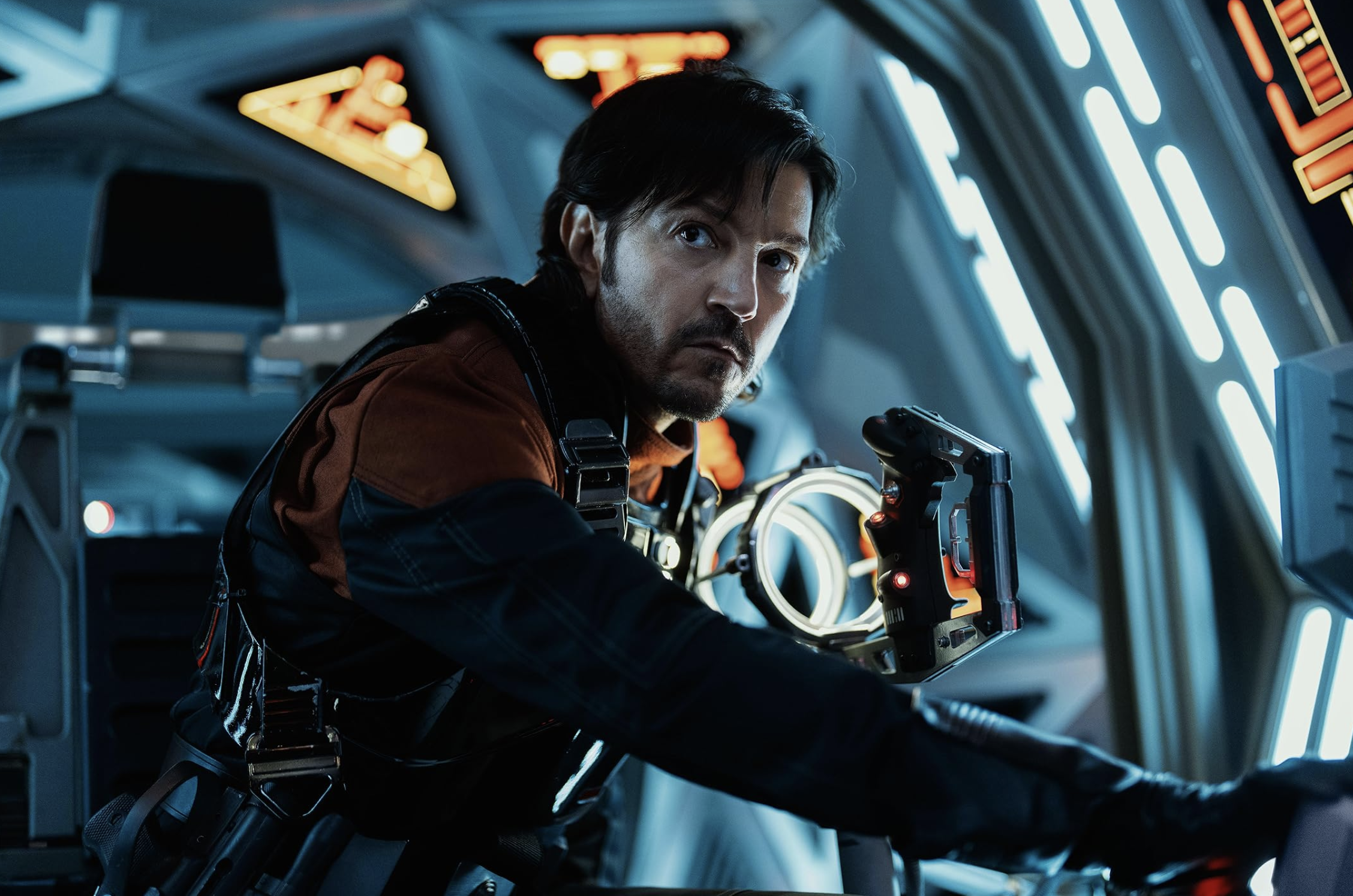 A man in pilot gear leans against the wall of a space ship.