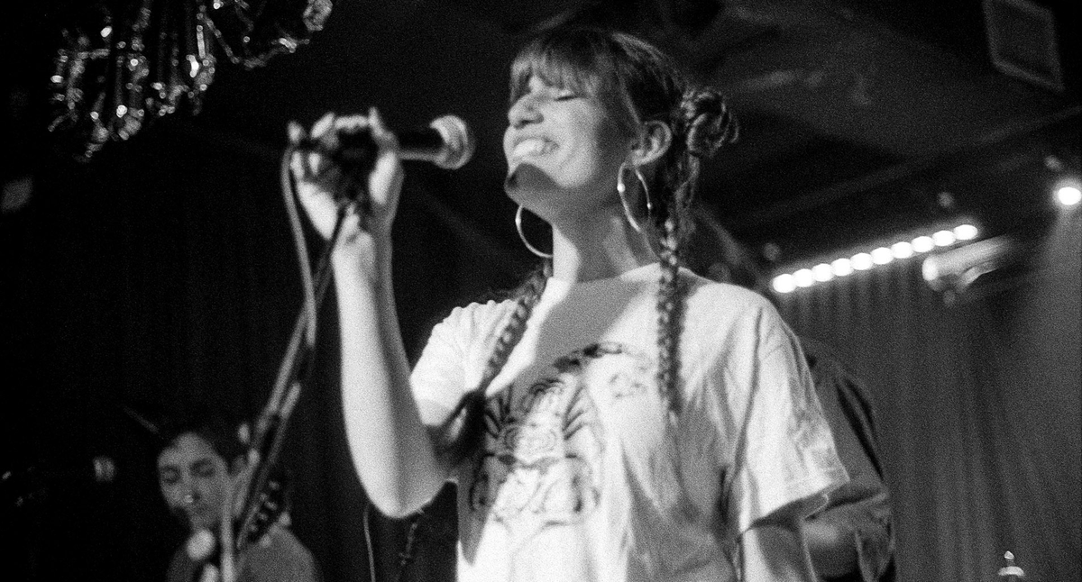 Lexee wearing her own LXE band merch, an off-white coloured teeshirt with a funky patterned scorpion illustrated on the front, designed by Iris Xie and printed by Lady Killer Press