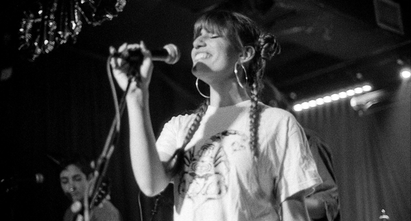 Lexee wearing her own LXE band merch, an off-white coloured teeshirt with a funky patterned scorpion illustrated on the front, designed by Iris Xie and printed by Lady Killer Press