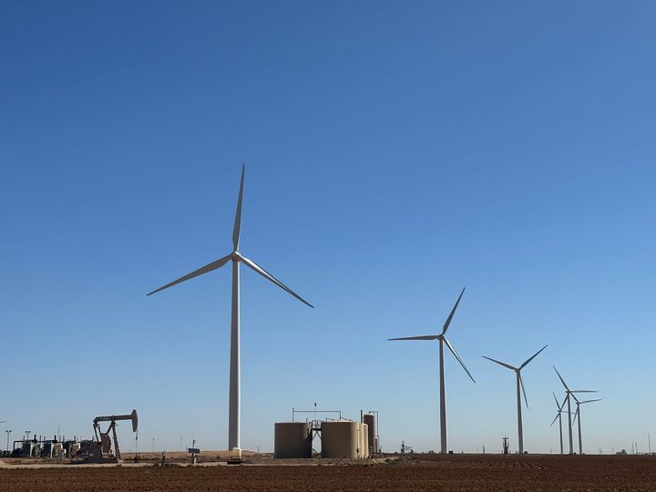 Image: Texas has the cheapest natural gas in the world. They choose wind power instead. A line of wind turbines towers over oil production equipment in Texas