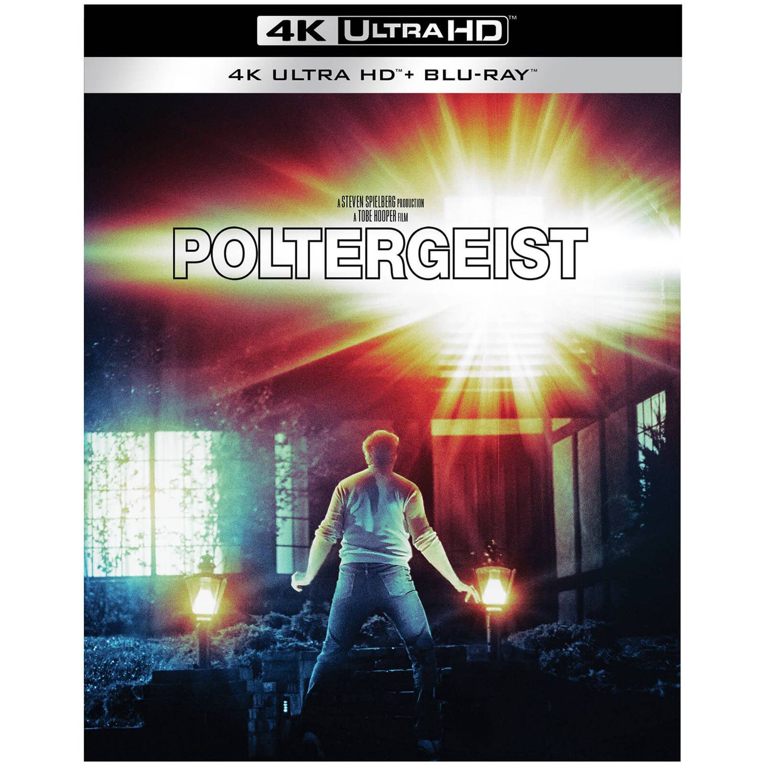 A man stands in front of a nondescript suburban home, light bursting from the upstairs window, in the cover art for Warner's 4K edition of POLTERGEIST.