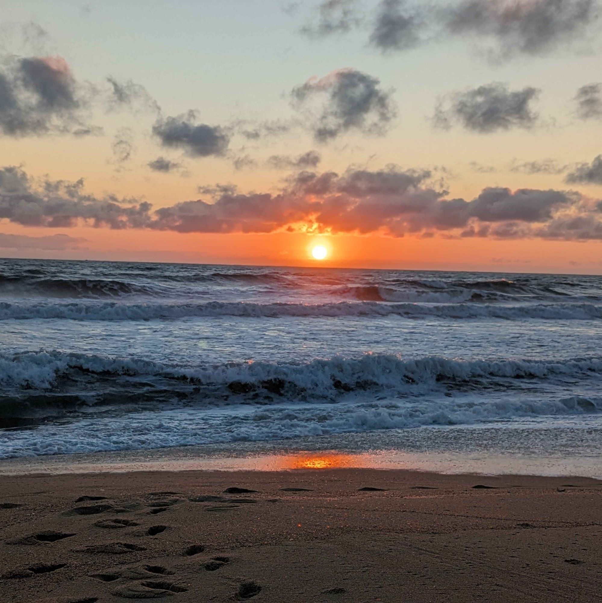 A sun rise over the Atlantic Ocean at the Outer Banks with footprints on the sand.