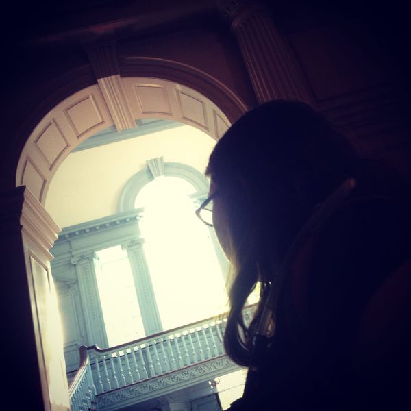 A woman in glasses is looking out a large sun-filled window in Independence Hall.