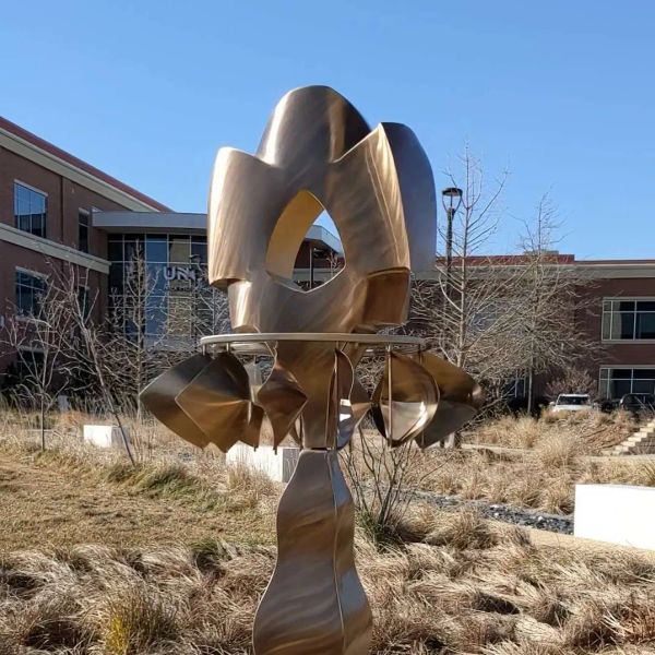 This is a photo of a copper-colored wind sculpture that is spinning around in circles in a garden.