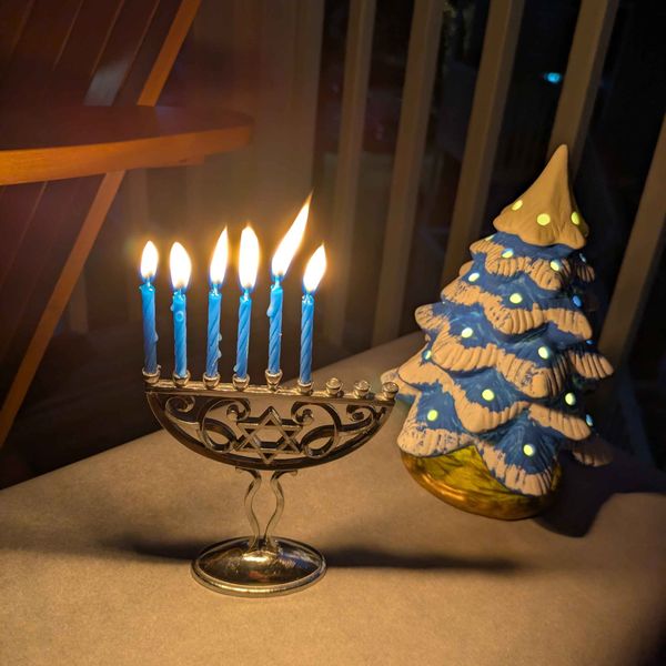 A lit menorah with six candles and a ceramic light up holiday tree sitting on a table.
