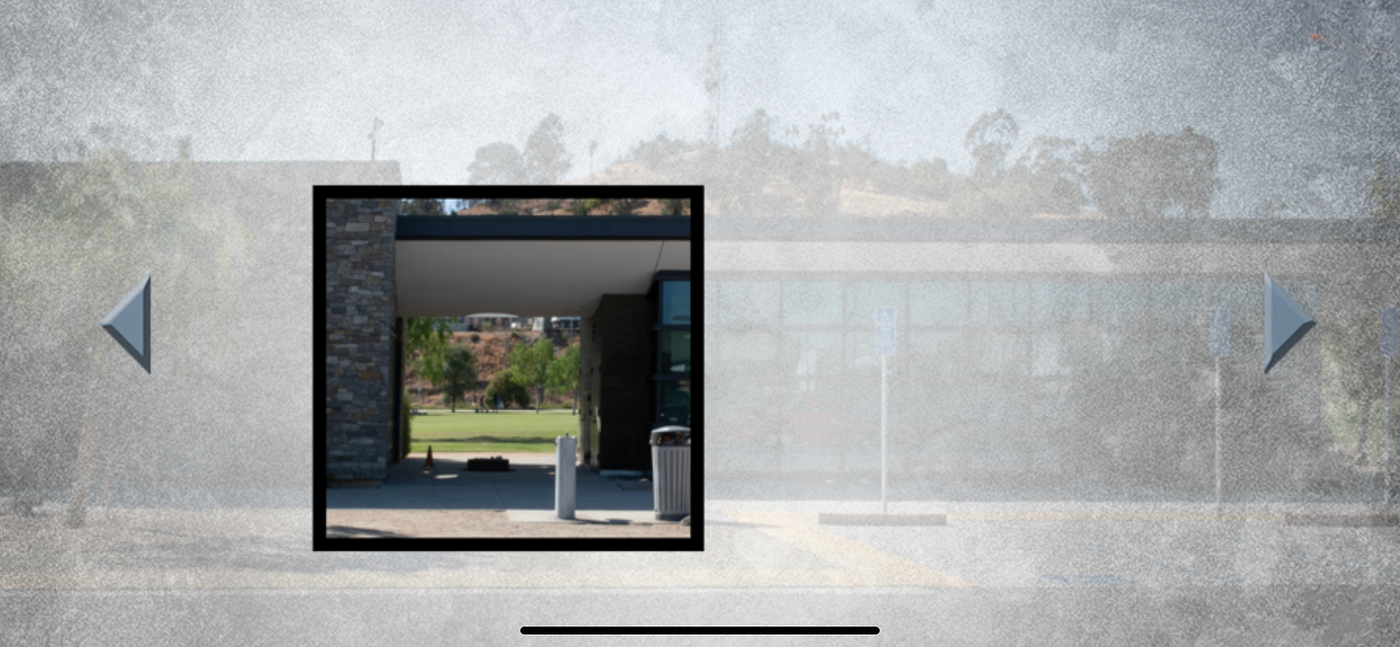 The image is a screengrab from a smartphone app. Most of the image is blurred, like a coating of frost over a window. The blurred image is a building with a walkway in front of it. Tree canopies peek out over the building’s roof. Close to the image’s center is a square, outlined in black. Inside the square is a clear, colorful portion of the the building and foliage. There’s a central, covered pathway. Through the portal a green field can be seen.