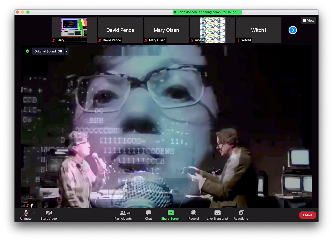 The image is a screenshot of a computer monitor. There’s a border of various instructions (“unmute,” “start video,” etc.). In the center are two people, facing each other. They’re in a darkened room, with electronic equipment surrounding them. One person is holding a microphone and the other cradles a small video camera. A projected image of the person with the microphone is magnified and superimposed, creating a surreal collage of imagery.