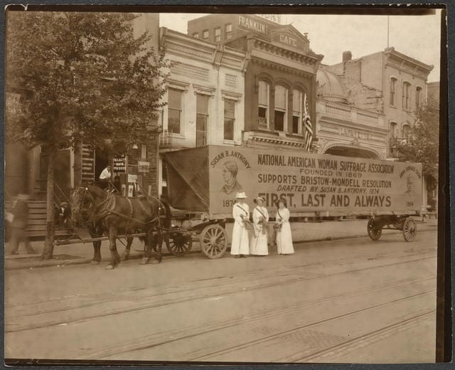 Suffragettes stand in front of a float declaring NAWSA support for the women’s suffrage amendment, 1914