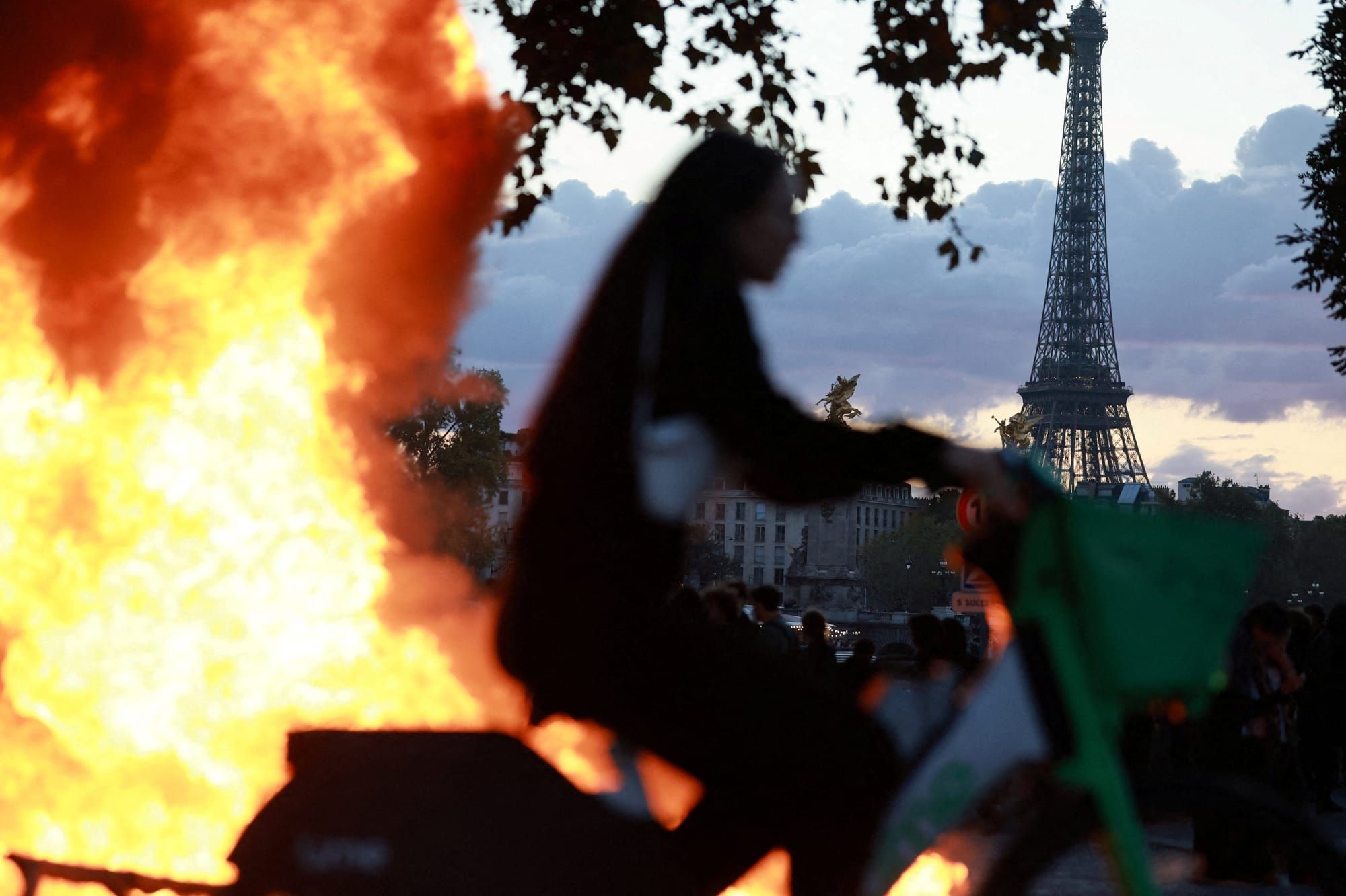 A woman rides a bicycle past a burning barricade near the Tuileries Garden with the Eiffel Tower in the background