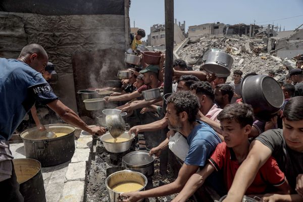 People reach out with pots during a food distribution in Jabalia Refugee Camp in Gaza City, Gaza | Photo by Abood Abusalama via Getty Images