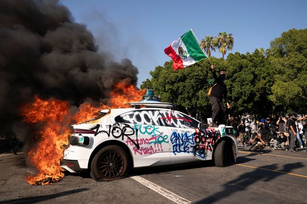A protester atop a burning Waymo vehicle in downtown Los Angeles, California — June 8, 2025 | REUTERS/David Ryder