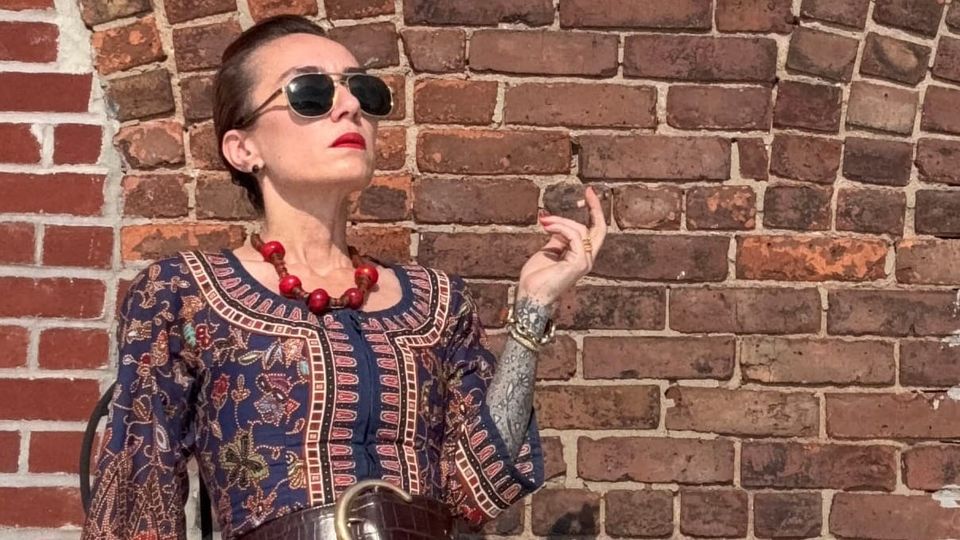 Woman in vintage batik kebaya seated against a brick arch, cigarette poised, gaze withheld. Rooftop ritual of composure and defiance