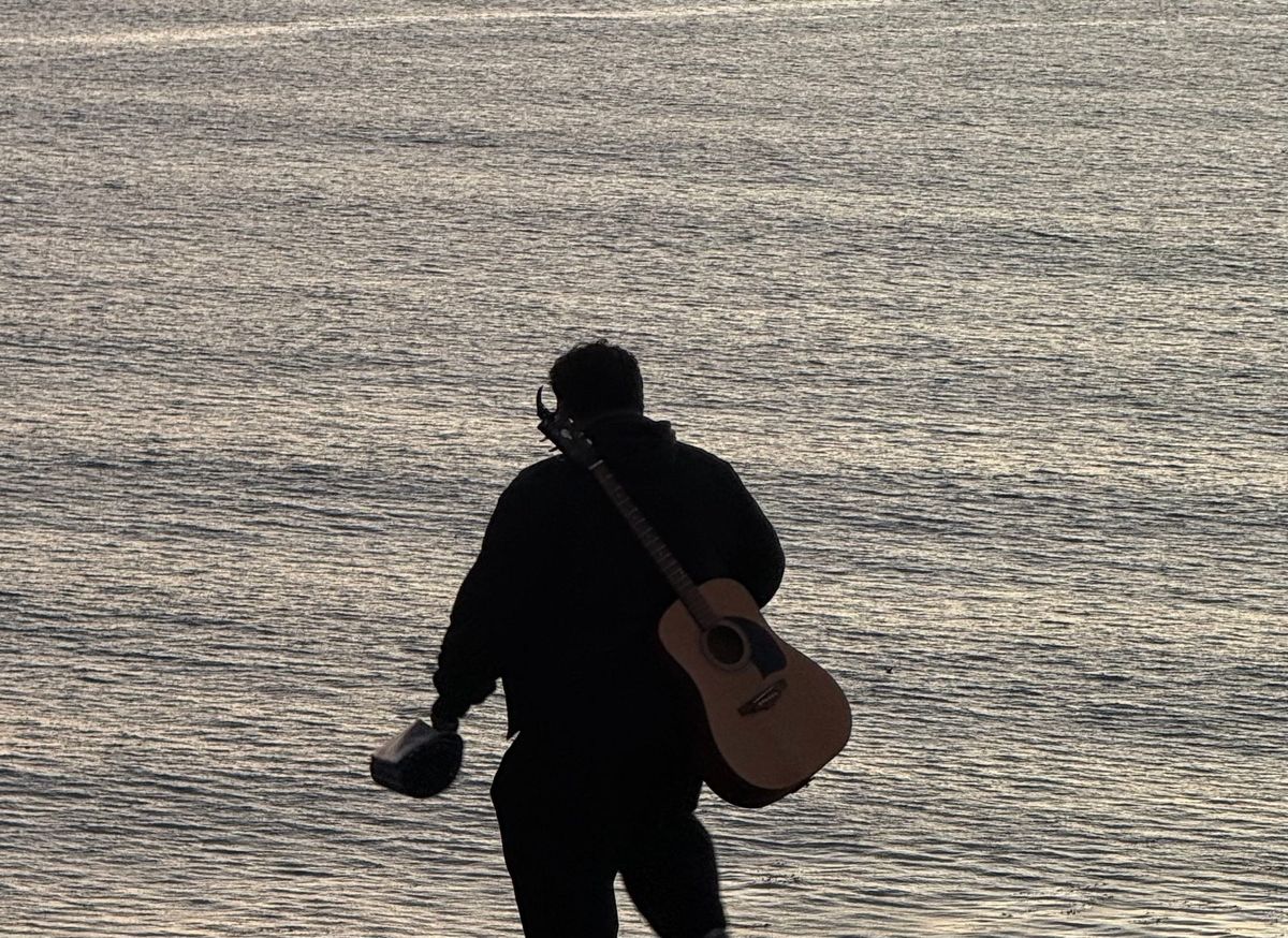 A man and his guitar form a silhouette against the ocean