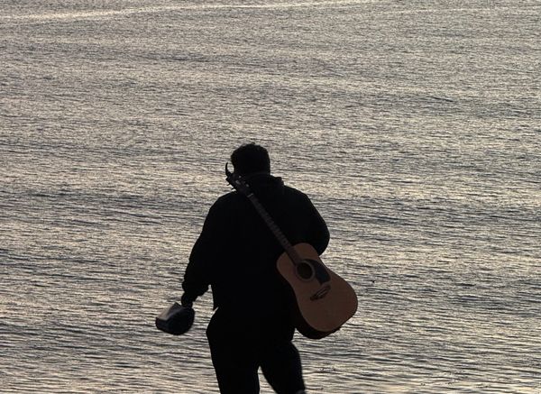 A man and his guitar form a silhouette against the ocean