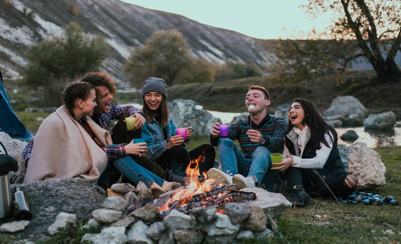 An image of couple of friends making marshmallows by the camp fire on a hiking trip in the mountains 