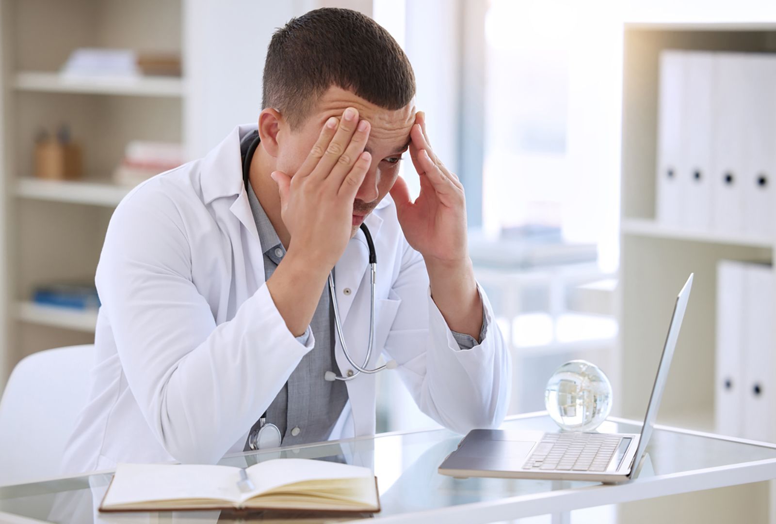 Doctor looking stressed at laptop due to stock management problems