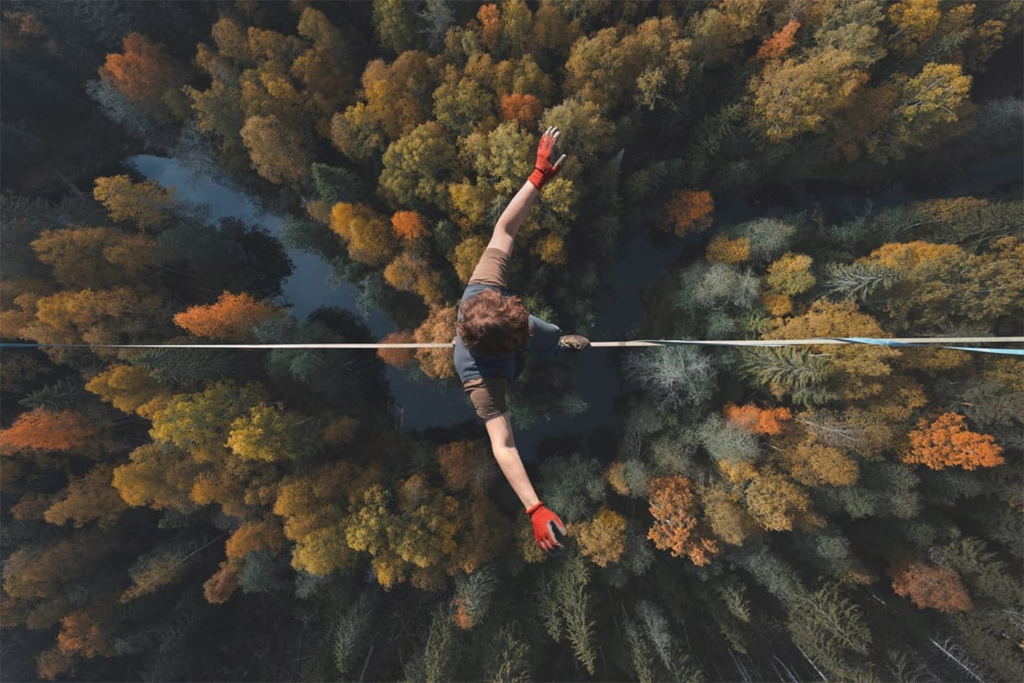 A breathtaking view of a tightrope walker walking along a line high above a beautiful forest. Topics of highline, longline, extreme activities. Top view.