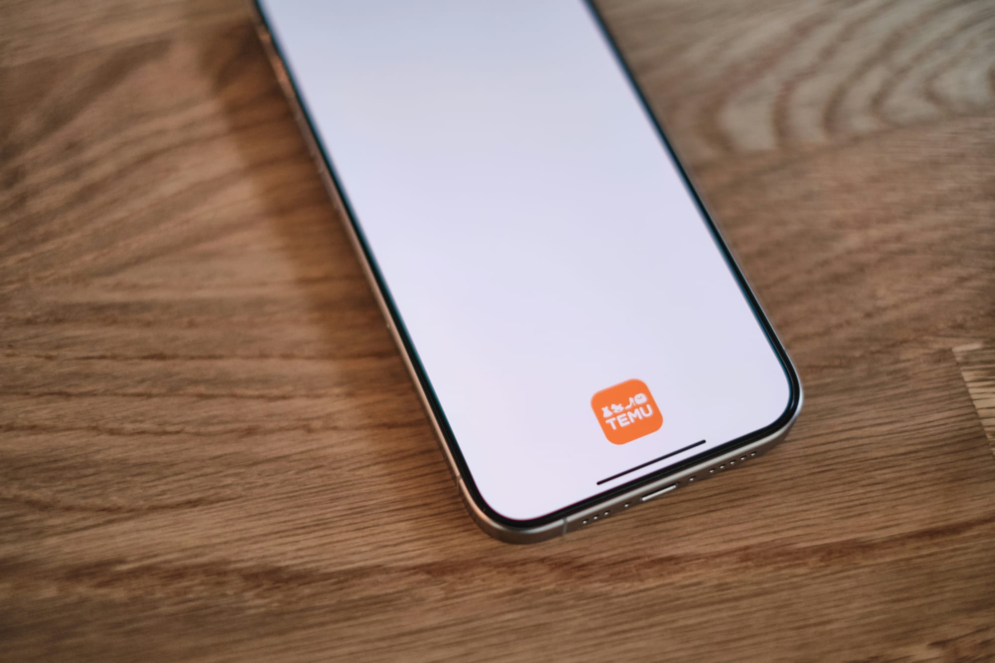 Smartphone displaying the TEMU app on a wooden surface.