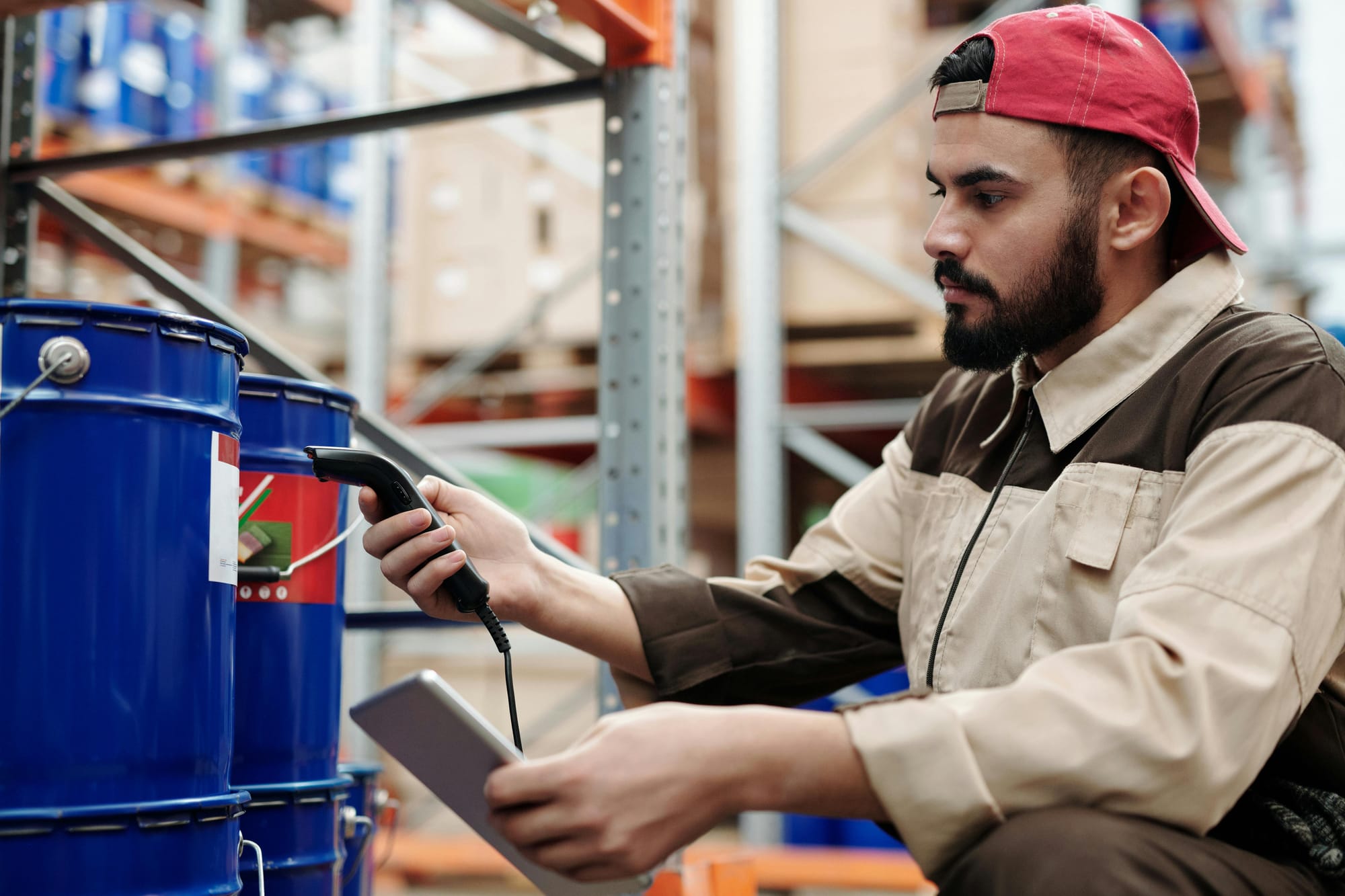 A person holding a barcode scanner and scanning a large tin can in a warehouse.