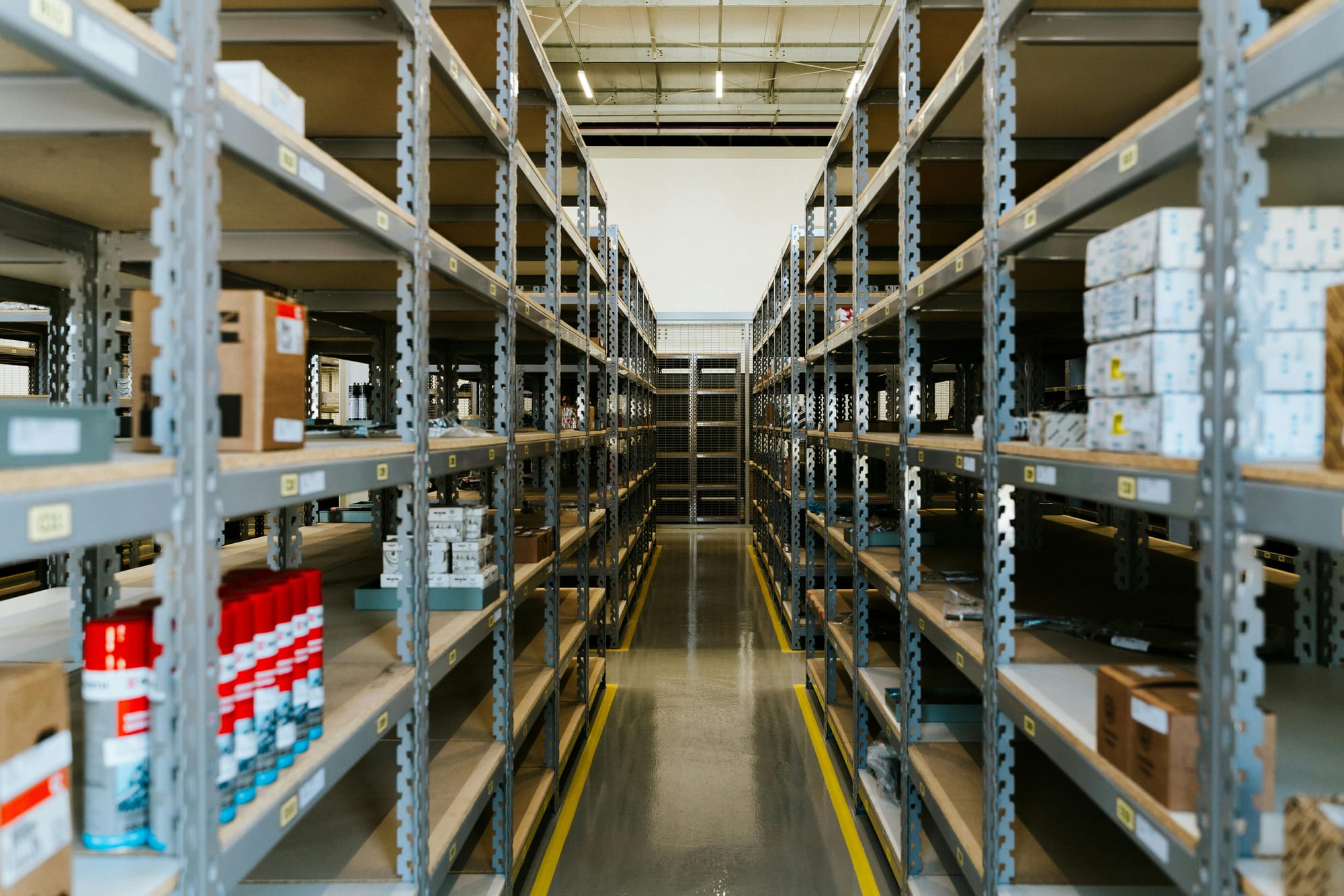 A warehouse aisle with metal shelves partially stocked with inventory and labeled storage boxes.