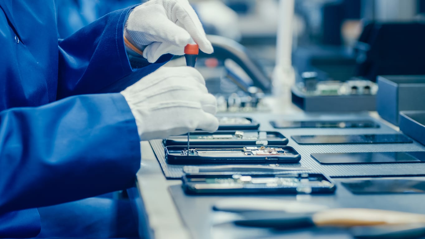 Close Up of a Female Electronics Factory Worker in Blue Work Coat and Protective Glasses Assembling Smartphones with Screwdriver